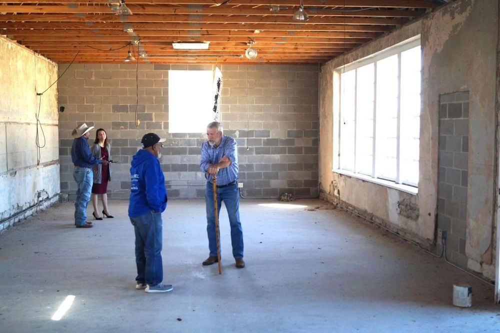 Visitors standing in the empty interior of the Lampasas Colored School under exposed wood beams, beside large windows