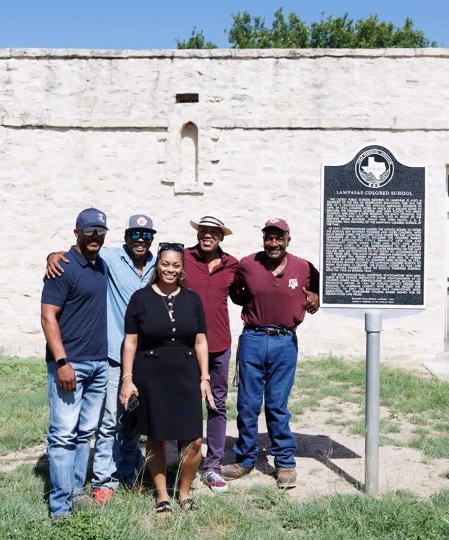 Five LCS team members standing together in front of the school wall and historical marker in August 2025